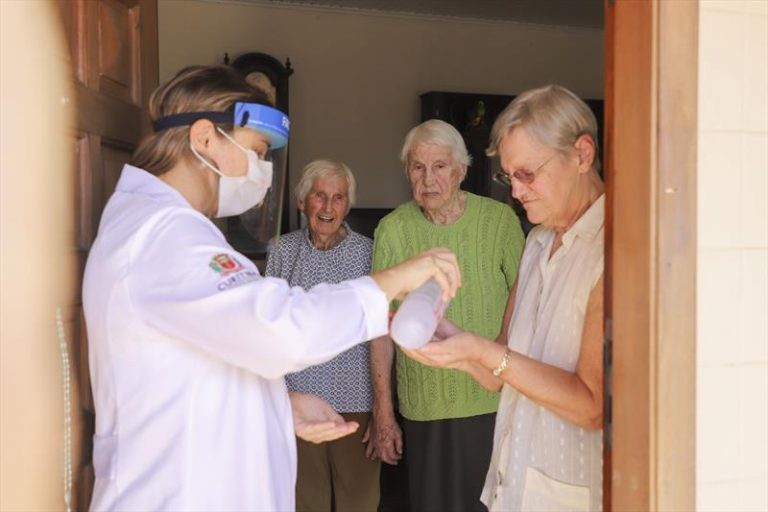 Profissional orienta idosos sobre uso do álcool 70% nas mãos - (Foto: Divulgação/Prefeitura de Curitiba)