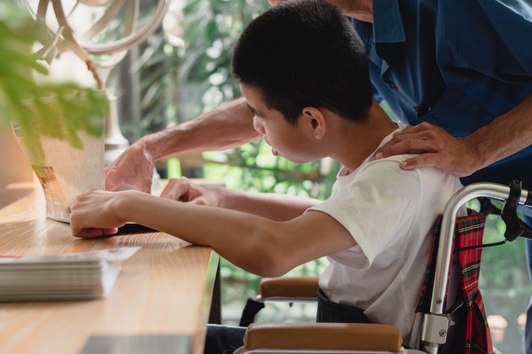 Adulto auxilia criança com deficiência a ler - (Foto: Depositphotos)